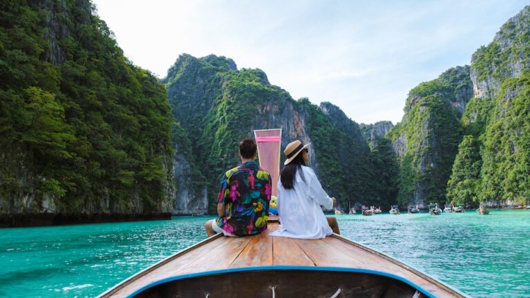 Couple sitting on a traditional longtail boat surrounded by limestone cliffs and turquoise sea in southern Thailand