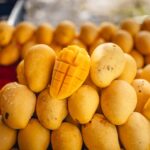 A ripe Nam Dok Mai mango cut open on a pile of golden mangoes at a Thai fruit stall