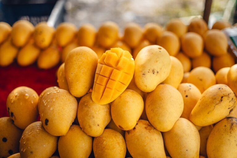 A ripe Nam Dok Mai mango cut open on a pile of golden mangoes at a Thai fruit stall