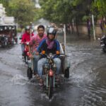 Three men ride a motorbike cart through a flooded street during the Thailand rainy season.