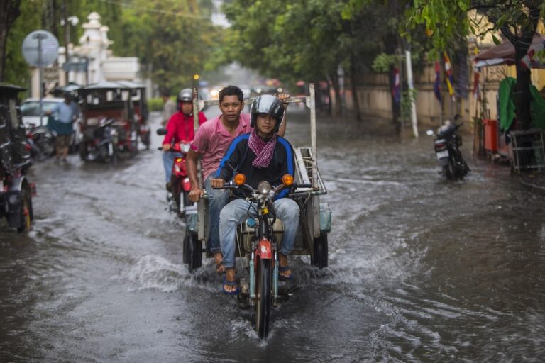 Three men ride a motorbike cart through a flooded street during the Thailand rainy season.
