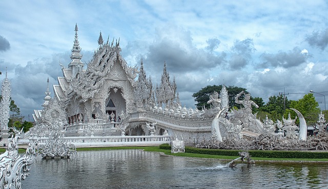 Wat Rong Khun, also known as the White Temple, in Chiang Rai, Thailand, with ornate white carvings and reflections in the water