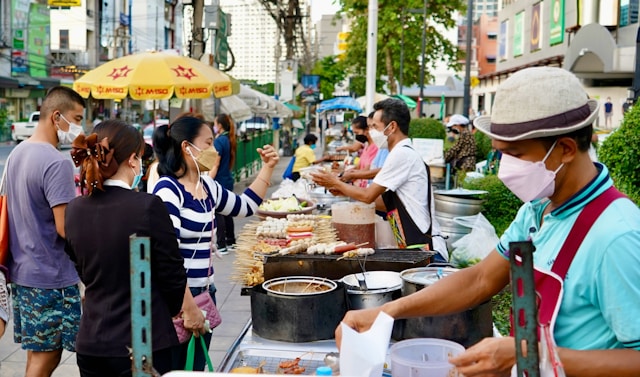 Locals wearing masks buying grilled skewers from street food vendors in Bangkok