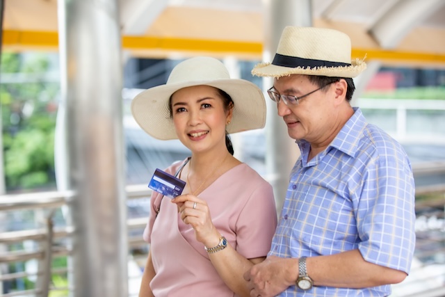 Smiling tourists holding a credit card in Thailand – a reminder to beware of ATM skimming and card fraud targeting travelers