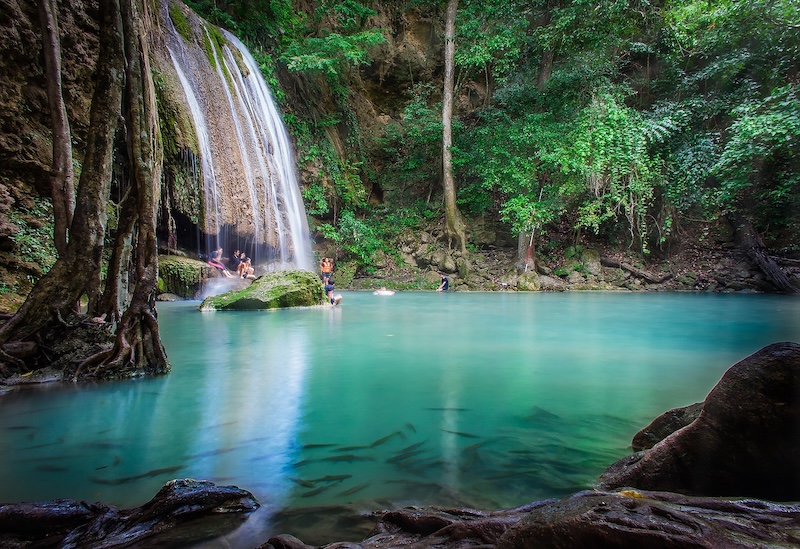 Emerald pool at Erawan Waterfall, Kanchanaburi, Thailand, with visitors swimming surrounded by lush jungle