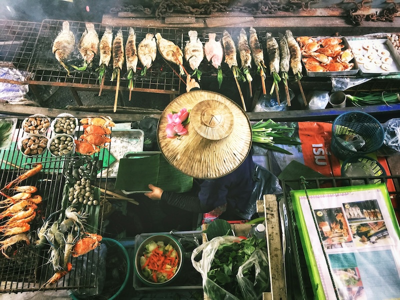 Overhead view of a Thai street food vendor grilling fish and seafood at a floating market