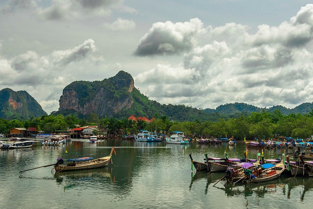 Traditional longtail boats anchored in calm waters under cloudy skies in Thailand during the monsoon season