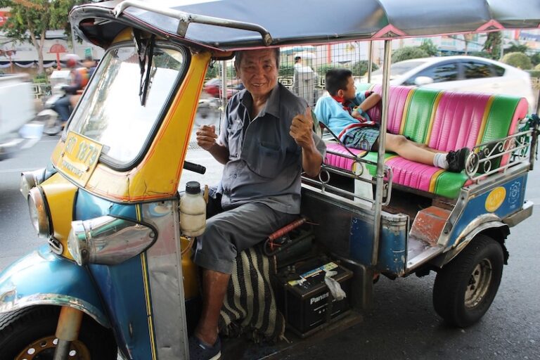 A friendly tuk-tuk driver gives a thumbs up in Bangkok while a child relaxes in the back seat.
