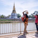 Two travelers pointing at a Thai temple across the river – commonly used in scams where tuk-tuk drivers claim the temple is closed