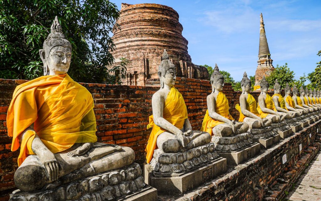 Row of stone Buddha statues draped in yellow robes at Wat Yai Chai Mongkhon, Ayutthaya, with ancient stupas in the background