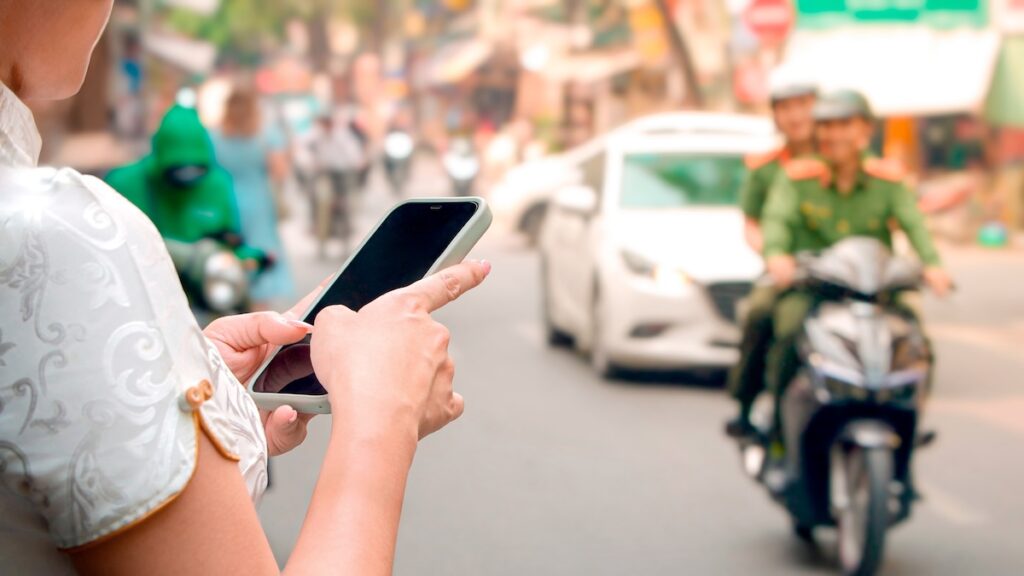 A woman in a traditional Vietnamese dress uses her smartphone on a busy street in Vietnam, symbolizing an expat facing a blocked bank account.