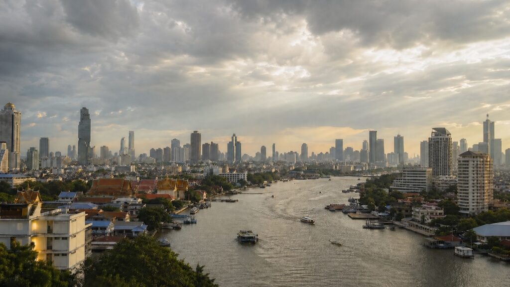Bangkok skyline and Chao Phraya River under a cloudy sky with sun rays