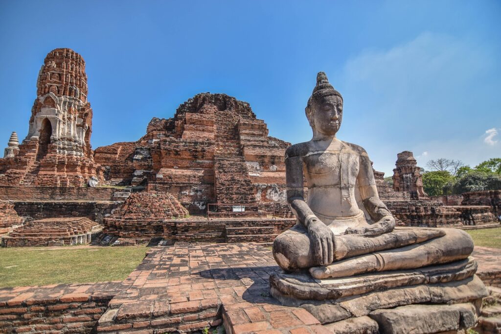 Stone Buddha statue in front of temple ruins at Wat Mahathat in Ayutthaya, Thailand.