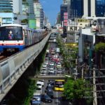 Train du BTS surélevé circulant dans un paysage urbain dense à Bangkok, avec une circulation routière intense en dessous.