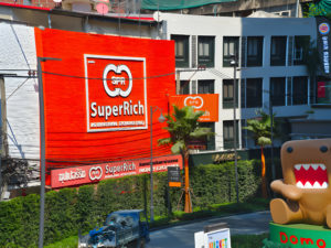 Grande enseigne publicitaire 'SuperRich' avec d'autres panneaux publicitaires et bâtiments urbains en arrière-plan.