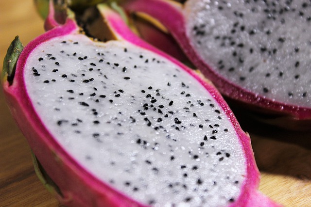 Fruit du dragon coupé en deux sur une planche en bois, montrant sa chair blanche et ses graines noires.
