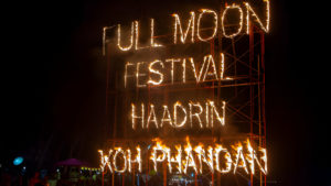 Enseigne enflammée du Full Moon Festival sur la plage de Haad Rin à Koh Phangan, avec les mots 'Full Moon Festival Haad Rin Koh Phangan' illuminés par le feu.