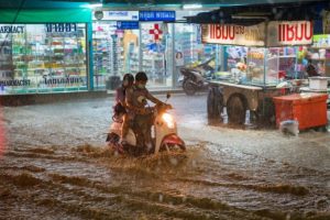 Deux personnes à moto traversant une rue inondée la nuit devant une pharmacie.