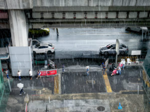 Personnes marchant sous une pluie battante à côté d'une station de taxi et de véhicules stationnés.