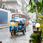 Tuk-tuk coloré circulant sous la pluie dans une rue animée de la ville.