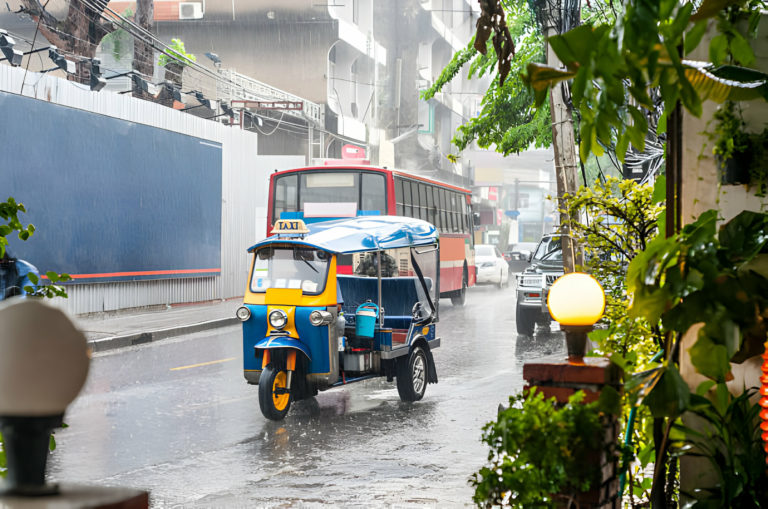 Tuk-tuk coloré circulant sous la pluie dans une rue animée de la ville.