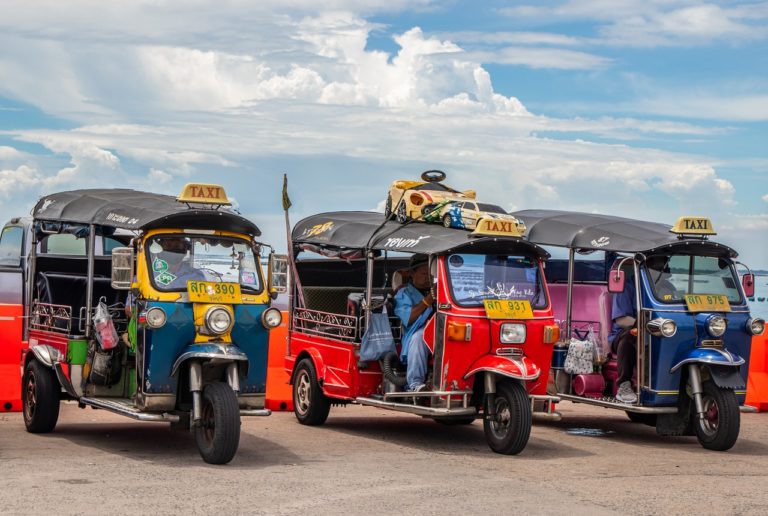 Trois taxis Tuk-Tuk colorés en attente de clients, avec un chauffeur assis dans le véhicule central.