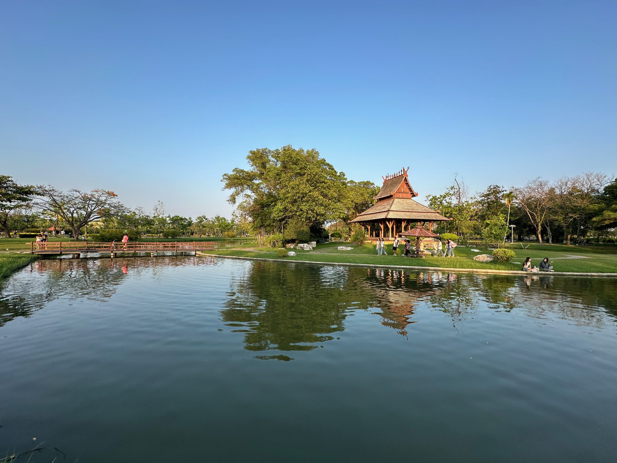 Pavillon traditionnel thaïlandais et visiteurs se reflétant dans l'eau au Parc Suan Luang Rama IX, Bangkok