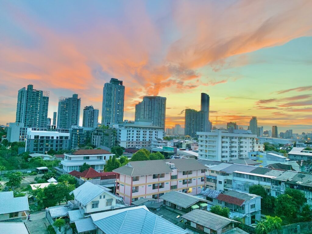 Vue panoramique de l'horizon de Bangkok au coucher du soleil, montrant le contraste entre les gratte-ciels modernes et les maisons traditionnelles.