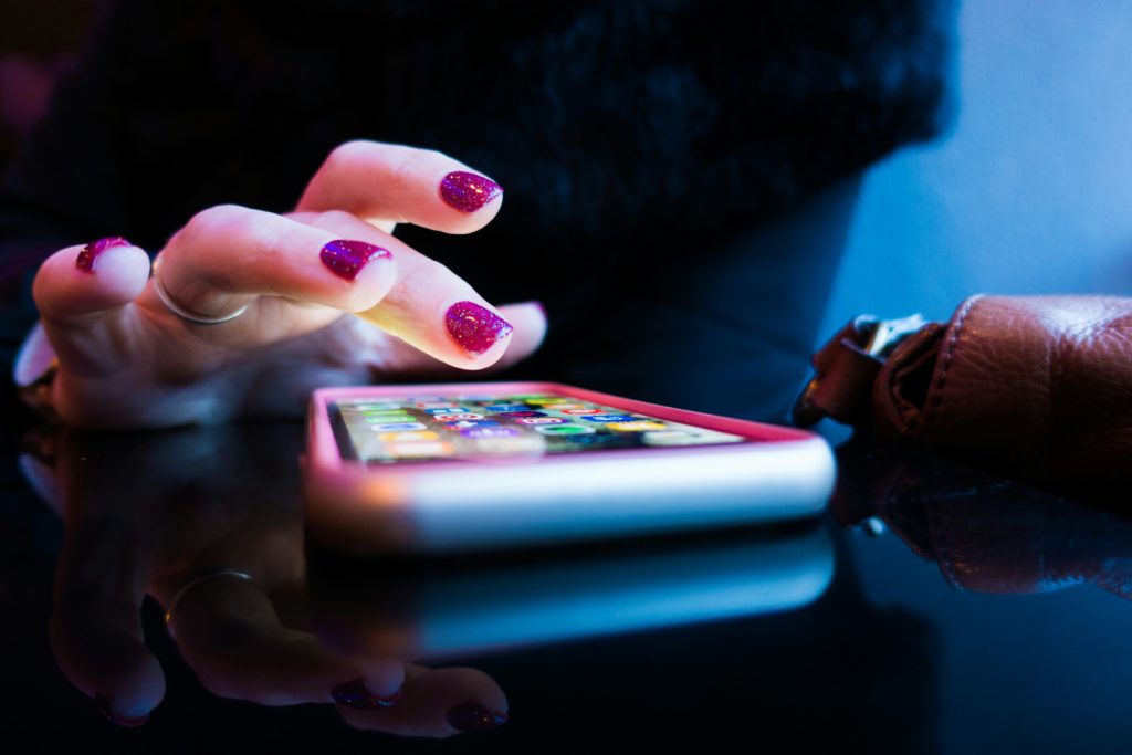 Gros plan sur une main avec du vernis à ongles violet pailleté utilisant un smartphone.