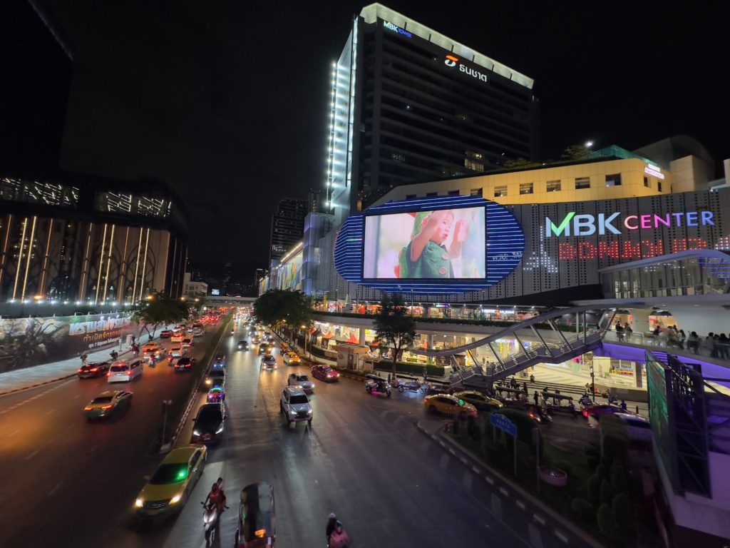 Vue nocturne animée du MBK Center à Bangkok avec trafic routier.