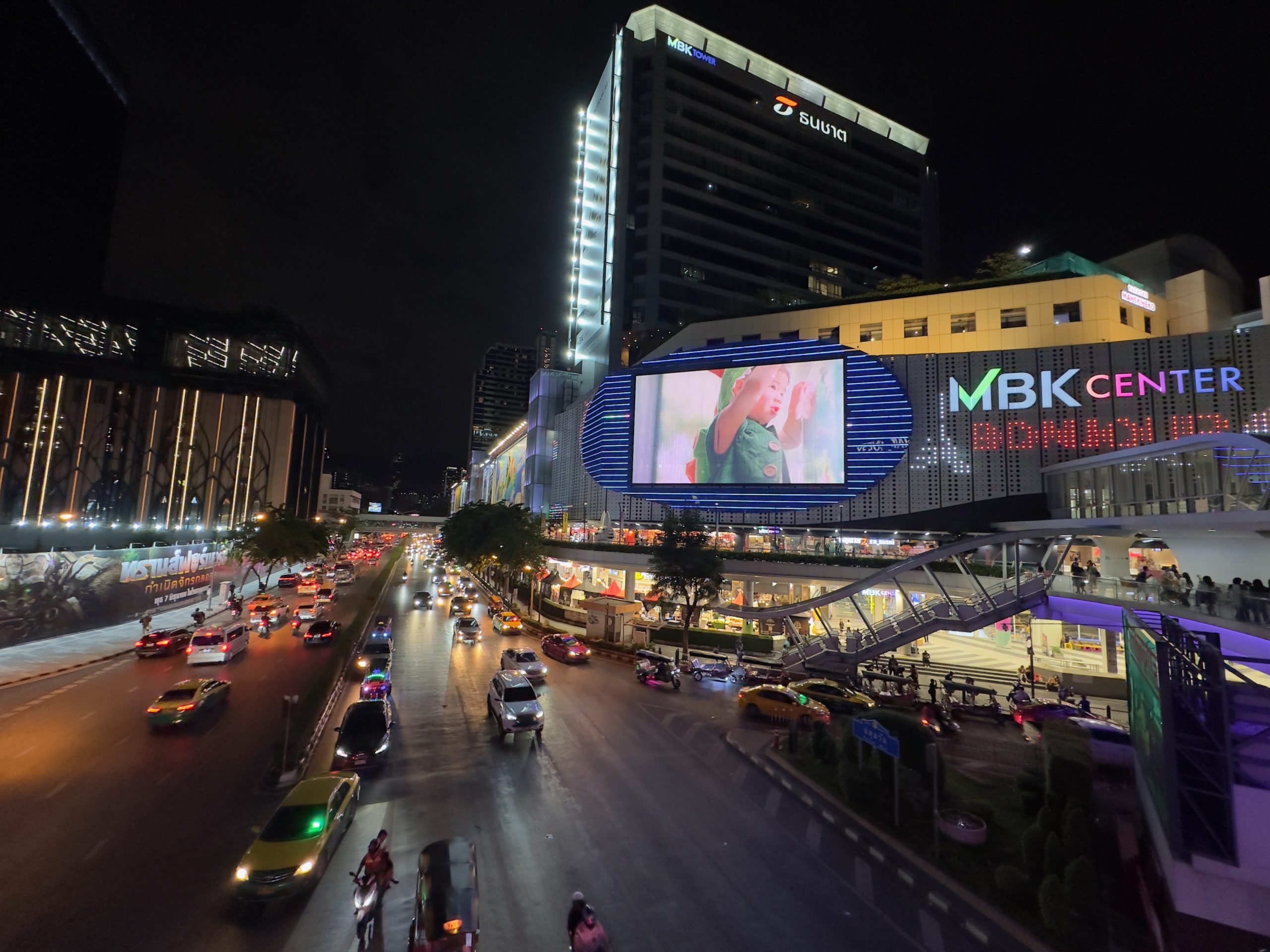 Vue nocturne animée du MBK Center à Bangkok avec trafic routier.