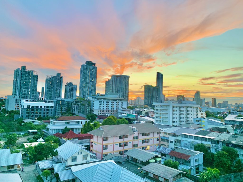 Vue aérienne du quartier de On Nut à Bangkok au coucher de soleil avec des bâtiments résidentiels et des gratte-ciel sous un ciel coloré.