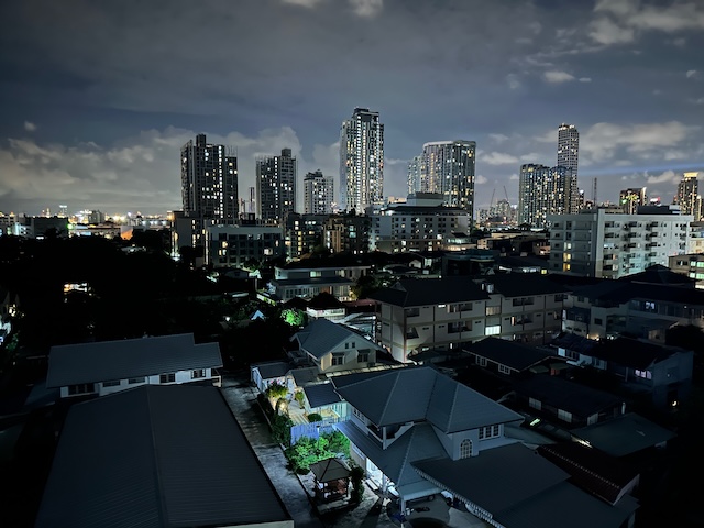 Paysage urbain nocturne du quartier On Nut à Bangkok, avec les gratte-ciels en arrière-plan et les maisons résidentielles typiques du quartier au premier plan.