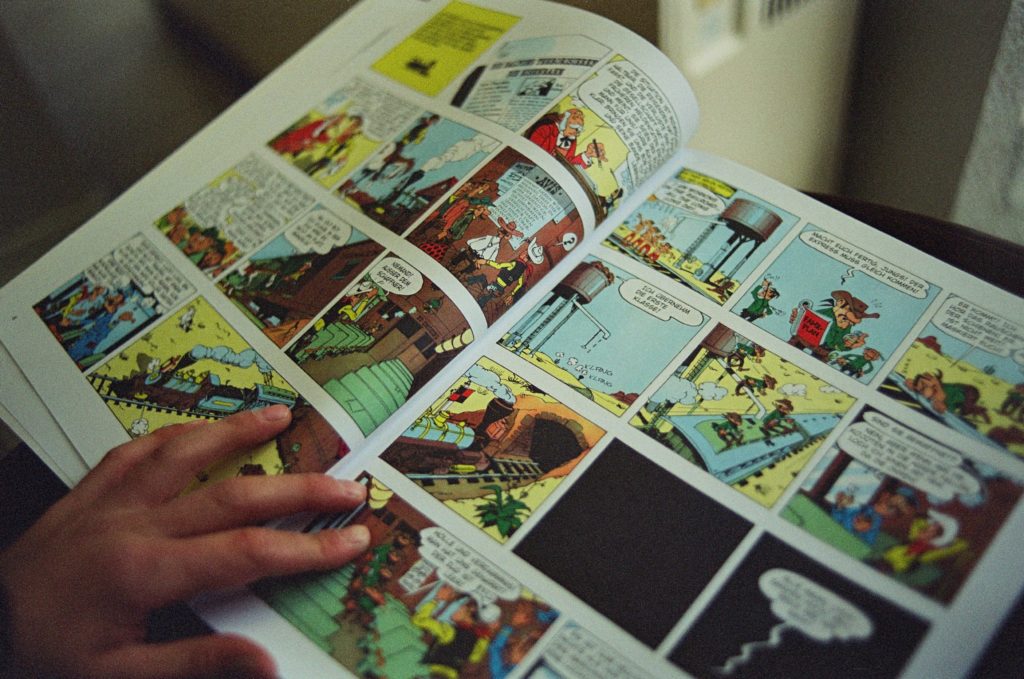 Main tenant une bande dessinée ouverte avec des cases colorées.