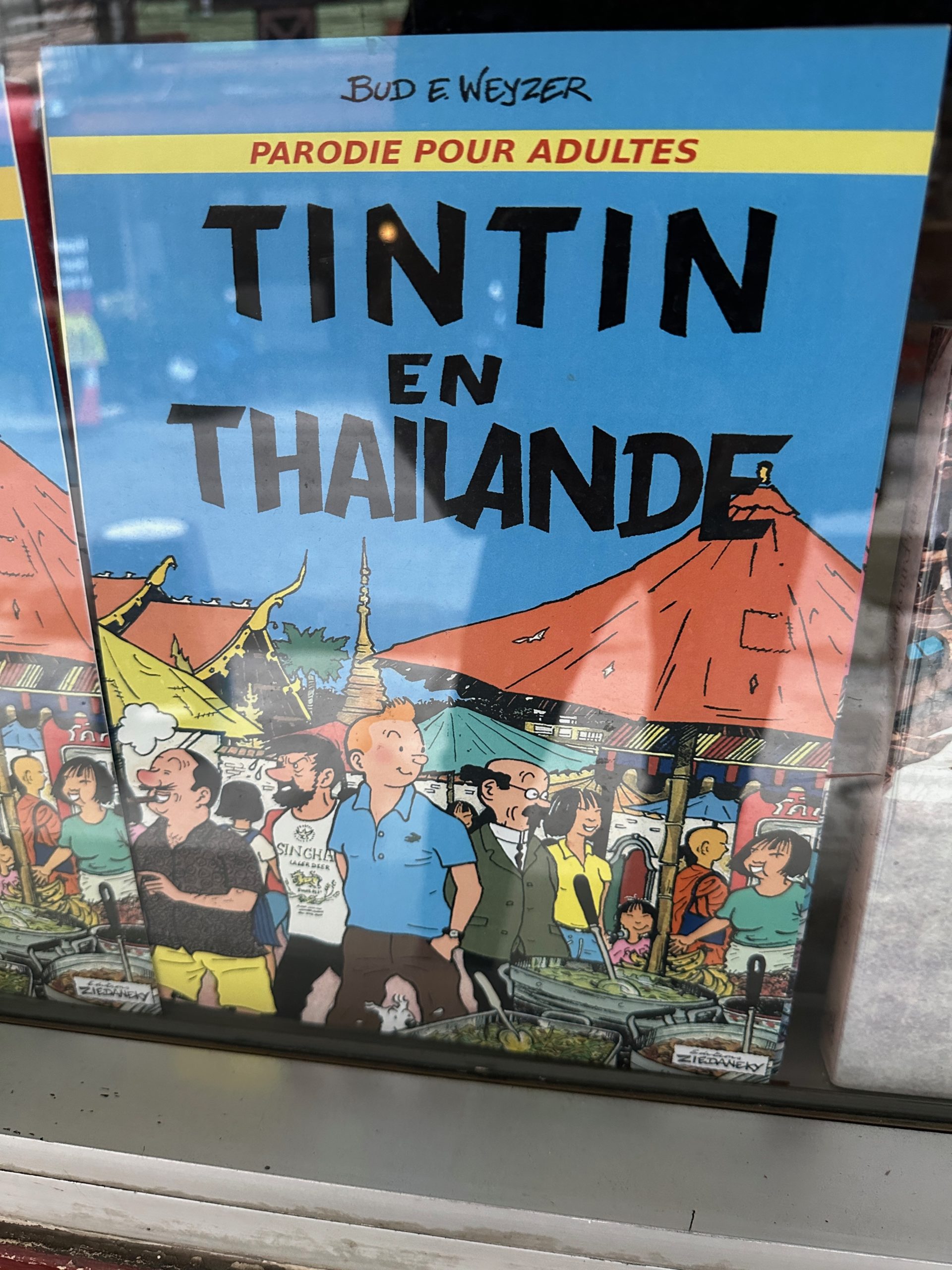 Couverture de bande dessinée parodique 'Tintin en Thaïlande' par Bud E. Weyzer exposée en vitrine.