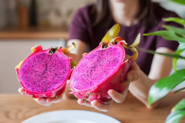 Fruit du dragon à chair rouge coupé en deux et présenté dans les mains d'une femme