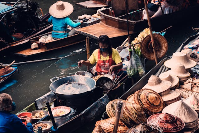 Vendeuse préparant un plat thaïlandais dans une barque au marché flottant