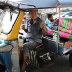 Chauffeur de tuk-tuk souriant, avec un jeune passager à l’arrière sur une route thaïlandaise