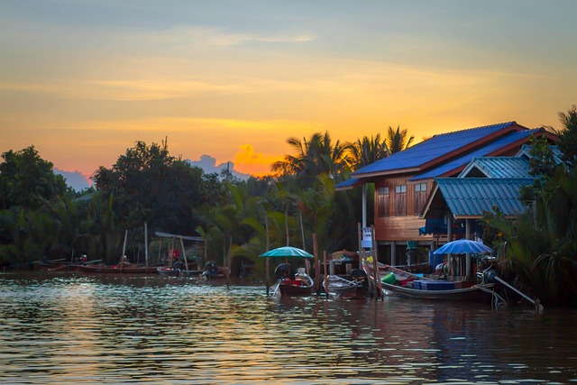 Maisons en bois et barques traditionnelles au bord d’une rivière en Thaïlande au coucher du soleil