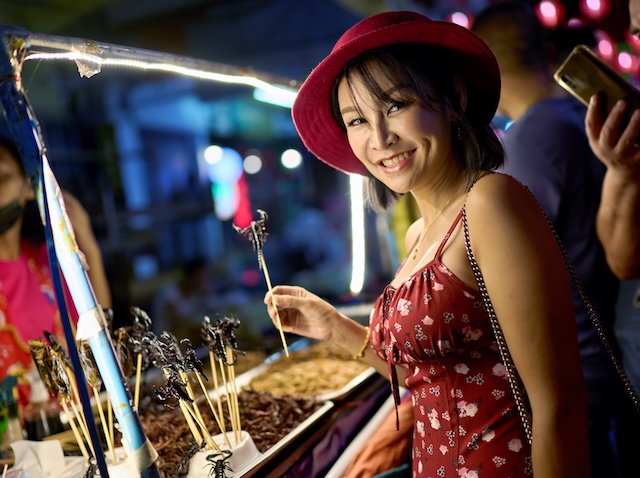 Jeune femme souriante goûtant un scorpion grillé dans un marché de nuit en Thaïlande