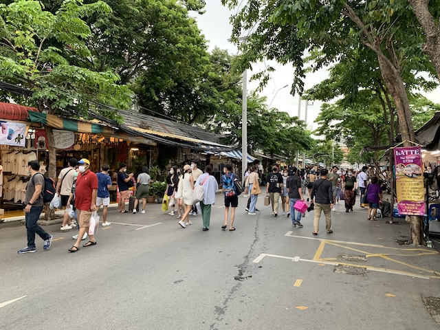Visiteurs marchant tranquillement entre les stands ombragés du marché de Chatuchak en fin de journée