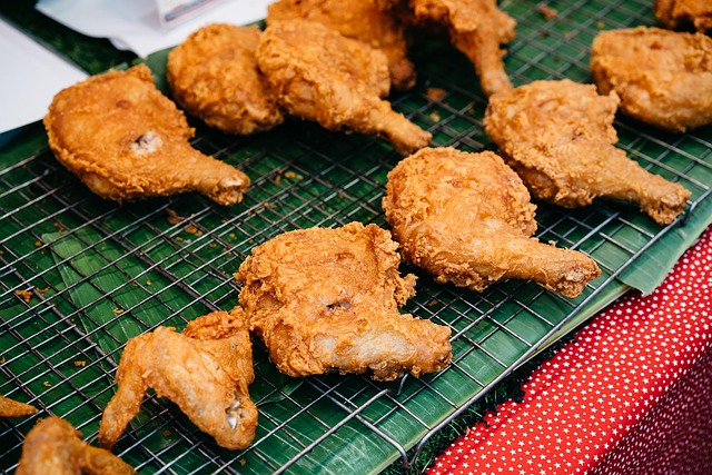 orceaux de poulet frit thaïlandais Gai Tod, dorés et croustillants, présentés sur une grille au-dessus de feuilles de bananier sur un stand de marché.