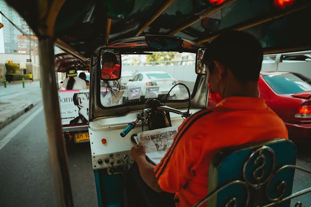 Vue depuis l’intérieur d’un tuk-tuk en Thaïlande, avec son conducteur lisant un journal