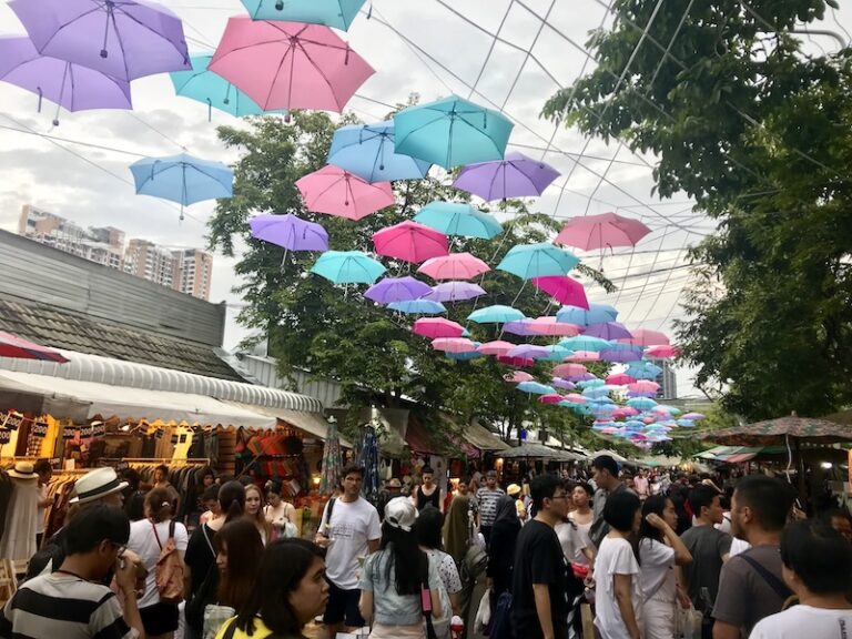 Allée du marché de Chatuchak avec des parapluies suspendus et foule animée à Bangkok