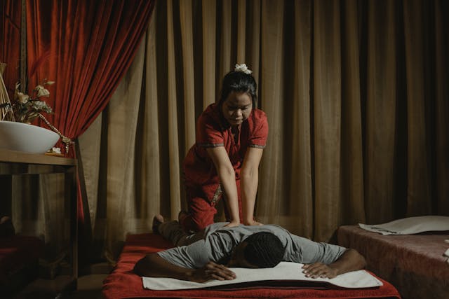 Femme en tenue traditionnelle pratiquant un massage thaïlandais dans un spa tamisé, activité idéale un jour de pluie
