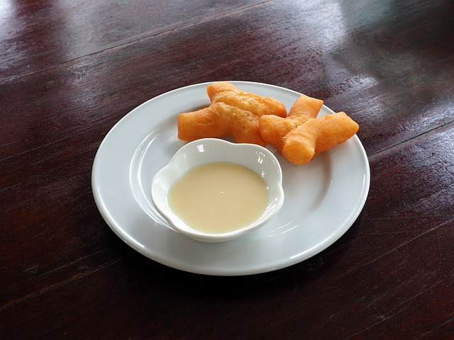 Beignets frits thaïlandais, Patongo, servis dans une assiette blanche avec une coupelle de lait concentré sucré.