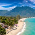 Vue aérienne de la plage de Lamai à Koh Samui, entourée de jungle et de montagnes sous un ciel bleu