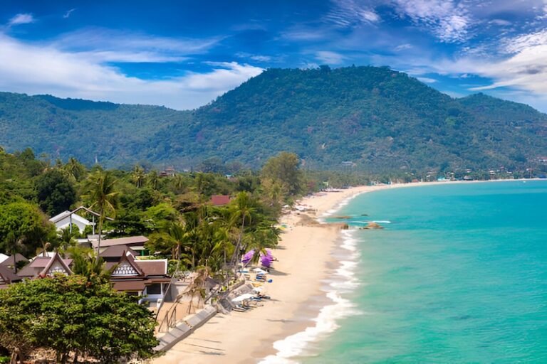 Vue aérienne de la plage de Lamai à Koh Samui, entourée de jungle et de montagnes sous un ciel bleu