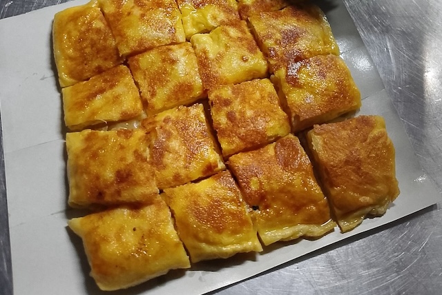Roti thaïlandais, un snack de rue sucré, doré et croustillant, coupé en carrés et servi sur un papier.