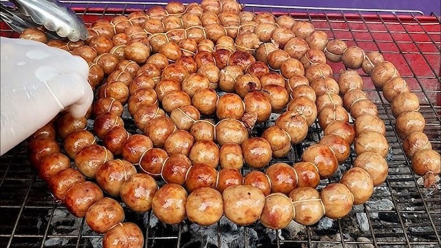 Saucisses fermentées Sai Krok Isan en train de griller sur un barbecue au charbon, un snack de rue typique du nord-est de la Thaïlande.